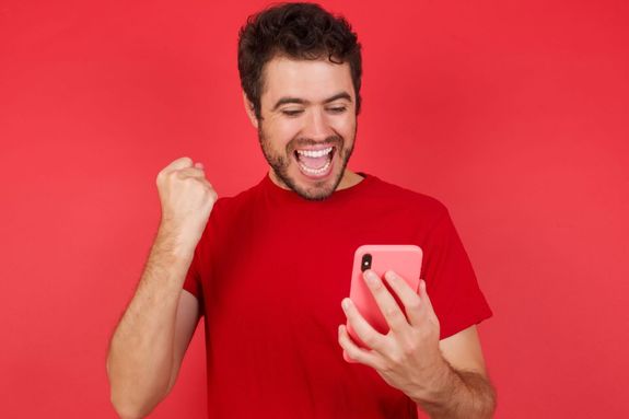 A man wearing red celebrating while holding a phone, against a red backdrop